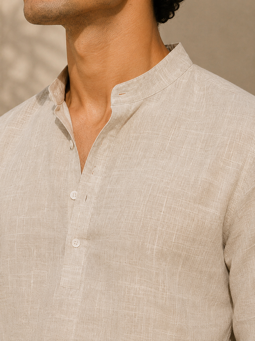 Close-up of a person wearing a beige linen shirt against a neutral background