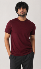 Man wearing a maroon t-shirt and dark pants against a plain background