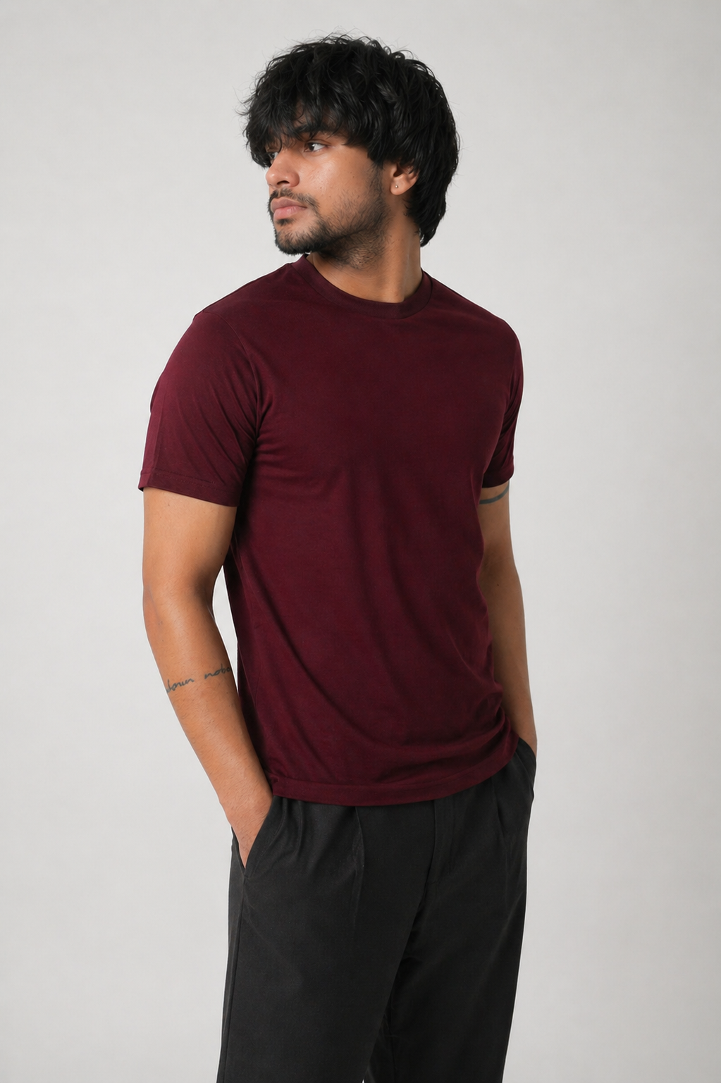 Man wearing a maroon t-shirt and black pants against a plain background