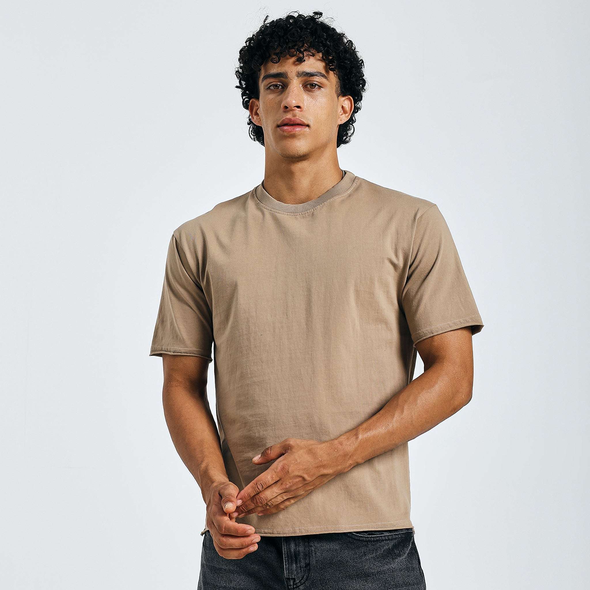 Beige minimalist graphic tee, front view, hands clasped, with naturally raw hems