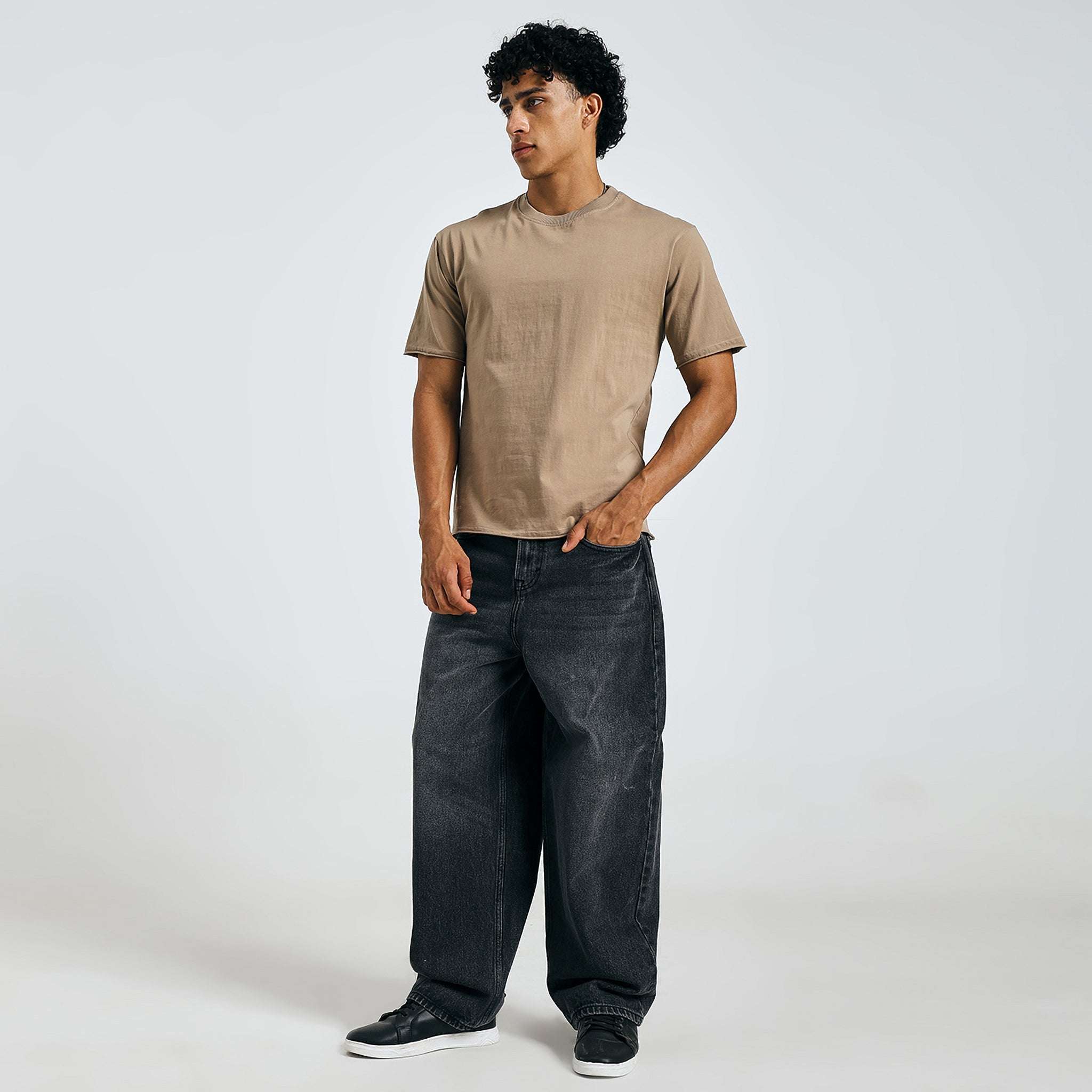 Shop beige minimalist graphic tee, front view, standing casually with black jeans.