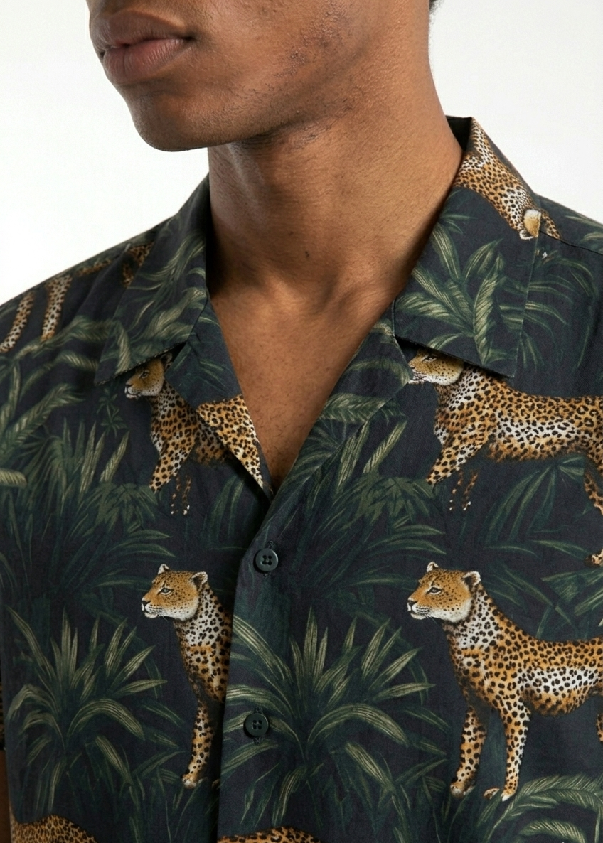 Person wearing a dark green shirt with a leopard and jungle leaf pattern.