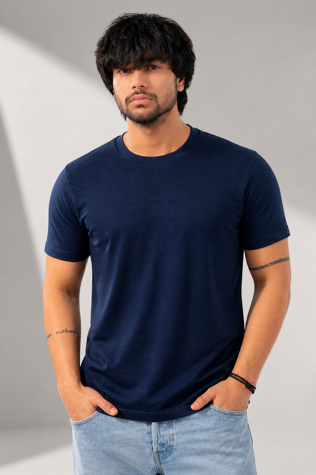 Man wearing a navy blue t-shirt and light blue jeans against a gray background