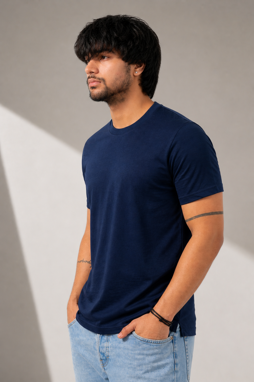 Man wearing a navy blue t-shirt and light blue jeans against a neutral background