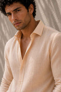 A close-up of a man wearing a light beige linen button-down shirt, showing the textured fabric and collar detail.