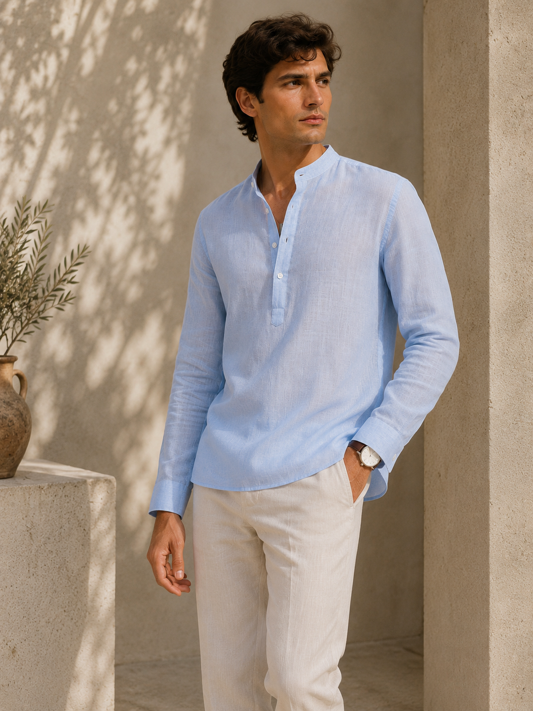 Man wearing a light blue shirt and beige pants standing against a beige wall.